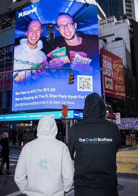 Josh and Chris Steil in Credit Brothers hoodies looking up at their own Times Square billboard